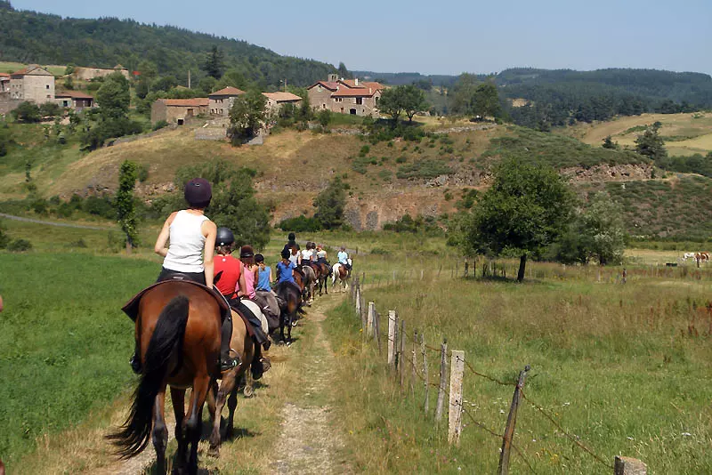 une dizaine de cavalier marchent au pas de leurs montures à la queue leu leu sur un chemin de campagne dans l'aveyron ; les cavaliers sont de dos, au fond on aperçoit un hameau de quelques maisons, puis des monts boisés