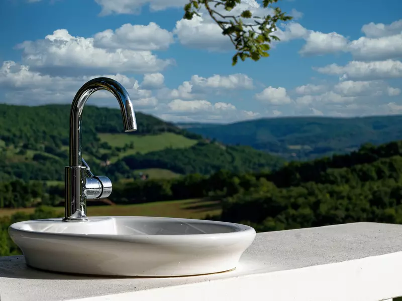 vasque évier de la cuisine extérieure du gite la cubane en quercy rouergue en gros plan ; en arrière plan, les vallons des gorges de l'aveyron dans un flou lié à la focale de l'objectif