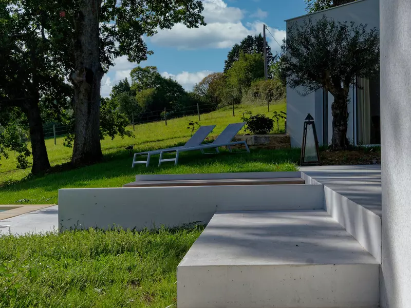 la terrasse du gite de la cubane en occitanie, architecture contemporaine ; en second plan, deux transat et un olivier ; en arrière plan, les prés et les bois