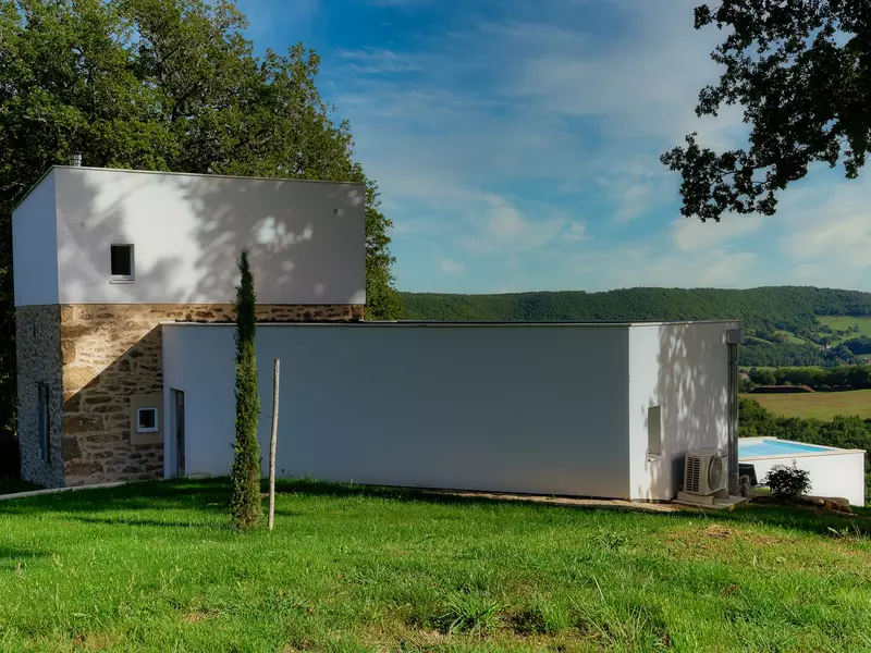 la façade nord du gite de la cubane proche des gorges de l'aveyron ; on voit l'aile centrale en deux niveau, pierre et enduit et l'aile ouest en un niveau, enduit blanc ; un if au premier plan