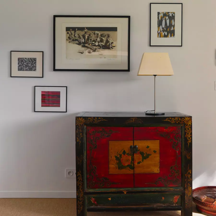 un meuble en bois peint, bordure noire délavée et porte rouge et jaunes décore l'une des chambres du gite de la cubane en tarn-et-garonne, région occitanie. quelques photos et lithographies au mur. Le tout a un côté élégant et sobre.
