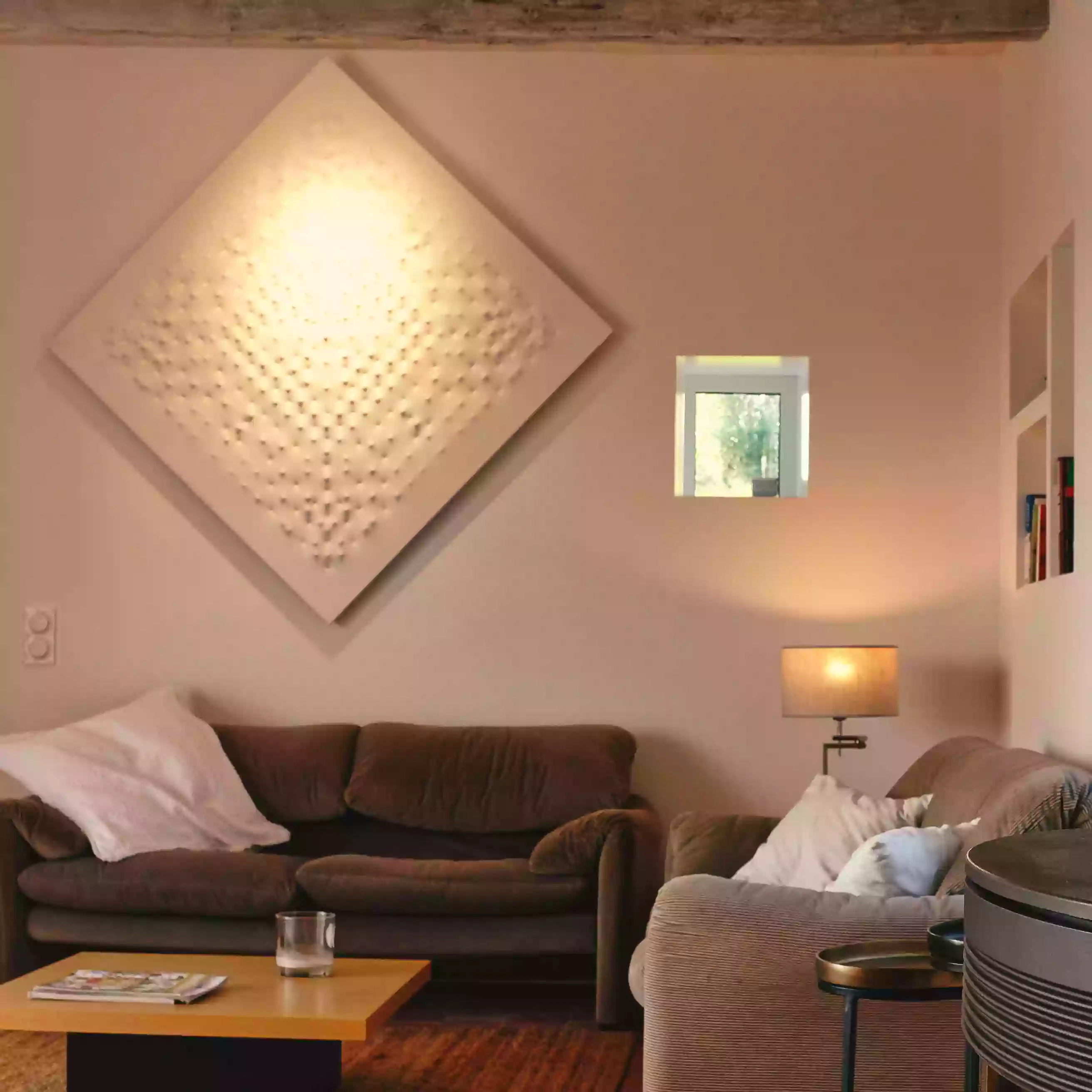 le coin salon du gite la cubane en tarn et garonne, avec canapés, tableau contemporain au mur, un petit fenestron qui permet de percevoir l'extérieur ; éclairage chaud d'ambiance